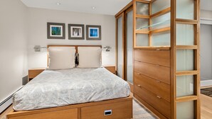 Een slaapkamer met een bed, een houten garderobe en drie ingelijste foto’s aan de muur.
