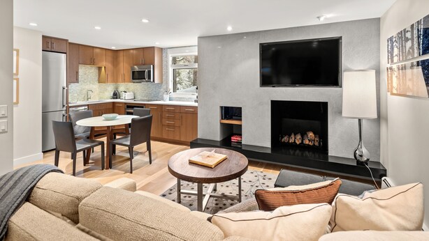 Een moderne woonkamer met een open haard, een flatscreen televisie aan de muur en een eethoek met een tafel en stoelen.