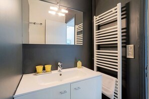 Ein modernes Badezimmer mit einem weißen Waschtisch, einem Spiegel und einem Handtuchhalter.