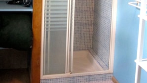 A shower with a glass door, a wooden ceiling beam, and a blue tiled wall.
