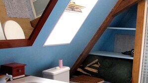 A bathroom with a wooden vanity, a white sink, a toilet, and a skylight.