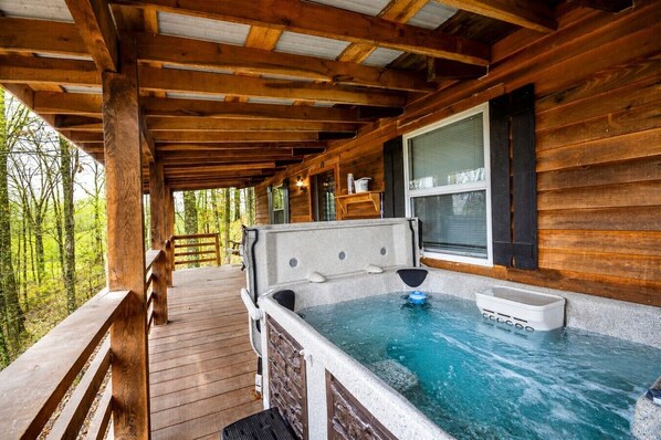 A wooden cabin with a hot tub on a wooden deck, surrounded by trees.