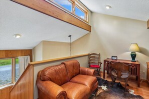 A cozy room with a leather sofa, a wooden chair, a small table with a lamp, and a view of the outdoors through a window.