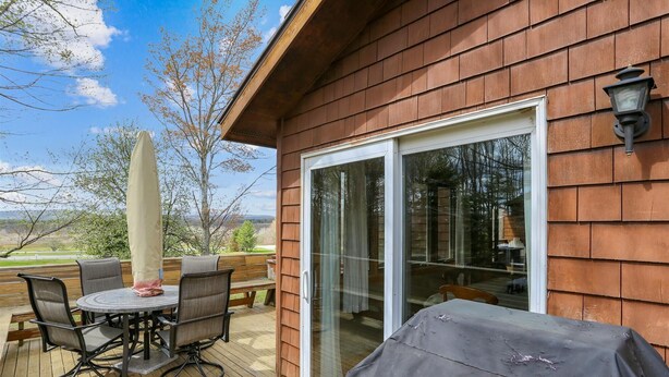 Une terrasse en bois avec une table et des chaises sous une pergola, une porte-fenêtre coulissante et une vue sur l’extérieur.