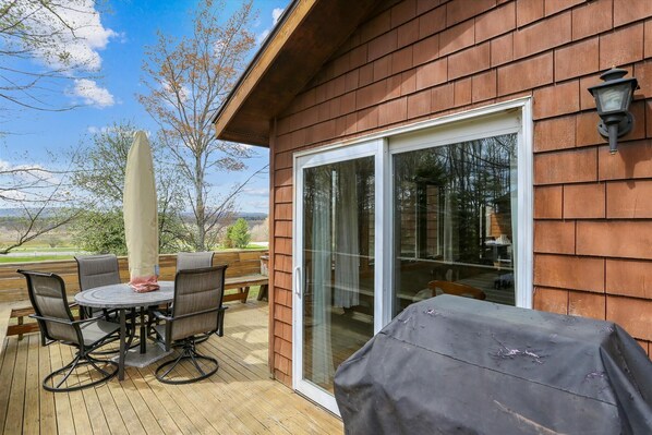 A wooden deck with a covered table and chairs, a sliding glass door, and a view of the outdoors. - Comfort and beautiful views combine to create GREAT! Come perch at Crows Nest (Canaan Valley)