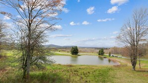 Un paysage paisible avec un étang, des arbres et une chaîne de montagnes à l’horizon.