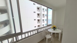Un balcon avec une table et des chaises blanches, un vase de fleurs et une vue sur un immeuble blanc doté de balcons.