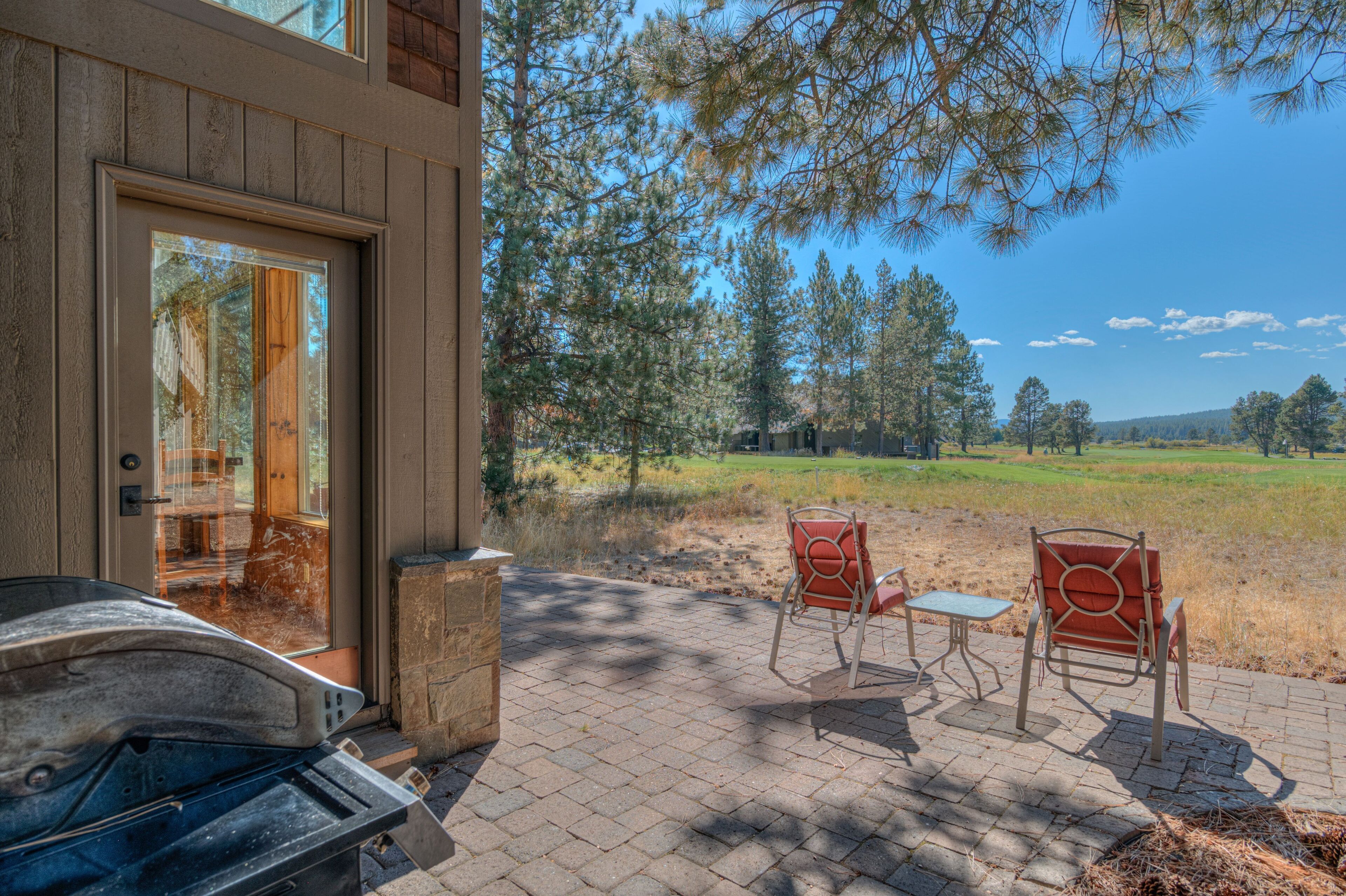 A patio with two chairs and a table, a stone wall, and a view of a grassy field and trees.