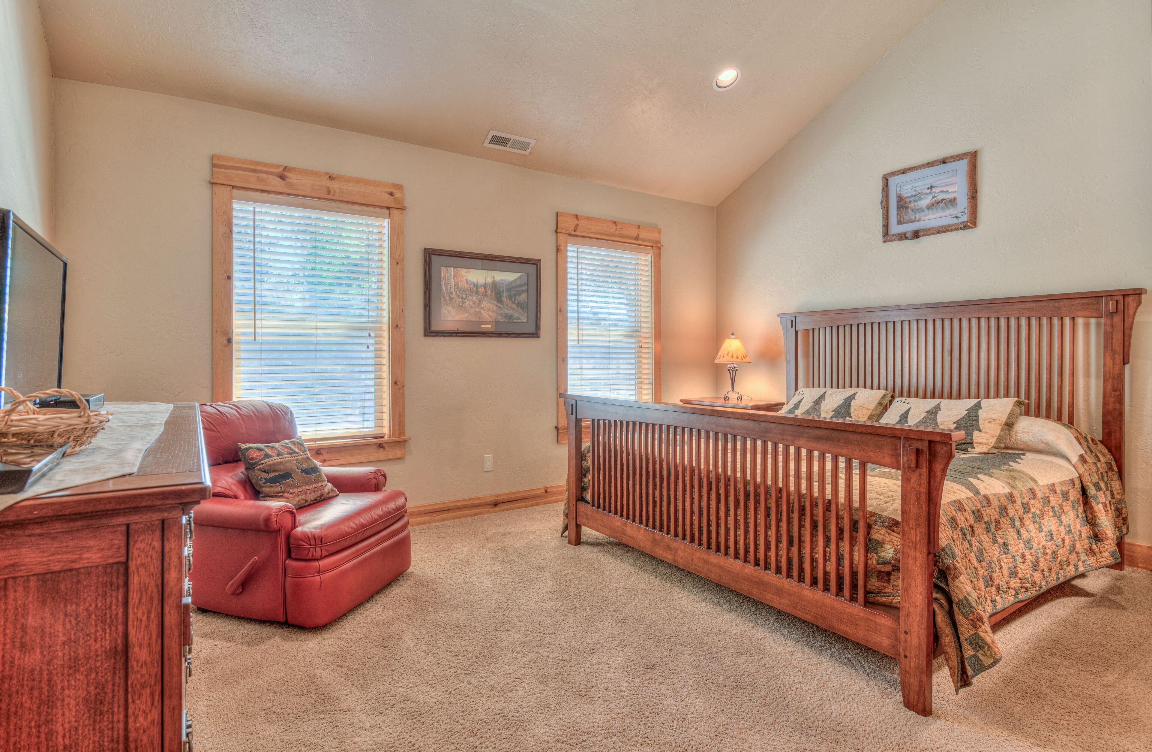 A bedroom with a wooden bed, a red leather chair, a desk, and a window with blinds.