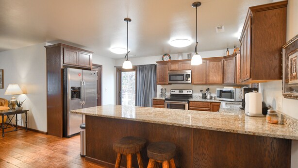 A kitchen with wooden cabinets, stainless steel appliances, a granite countertop, and two stools.
