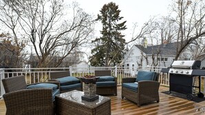 An outdoor deck with wicker furniture, a stone table, and a grill.