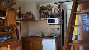 Eine Küche mit Holzschränken, einer Mikrowelle, einem Kühlschrank und einem Holzhocker.
