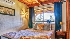 Un dormitorio con cama, mesita de noche, lámpara y ventana con cortinas.