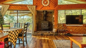 Interior acogedor de una cabaña con chimenea de piedra, paredes de madera y un ventanal con vistas a un bosque.