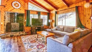 Un acogedor interior de cabaña de madera con chimenea de piedra, un televisor y un sofá.