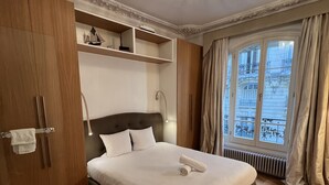 Ein Hotelzimmer mit einem großen Bett, einem Holzschrank, eingebauten Regalen, einer Kandelaberleuchte und einem fenster mit Vorhängen.
