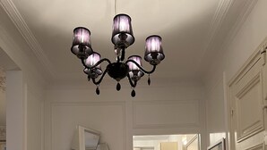 Ein Flur mit einem Chandelier, einem runden Tisch mit einer Lampe, einem Spiegel und einem Küchenbereich im Hintergrund.