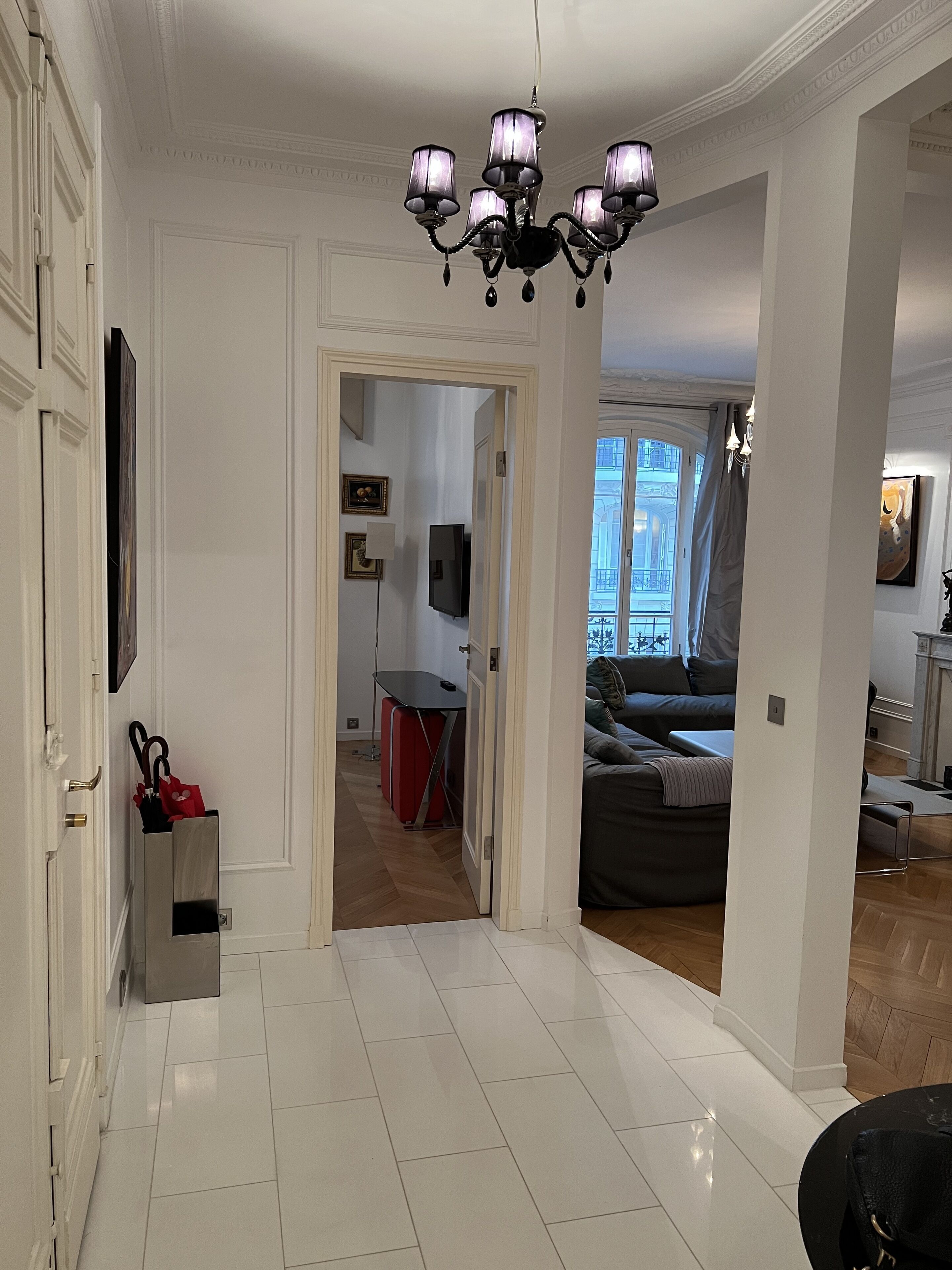 Un hall d’entrée spacieux agrémenté d’un lustre, un coin repas et un salon avec un canapé et une cheminée.
