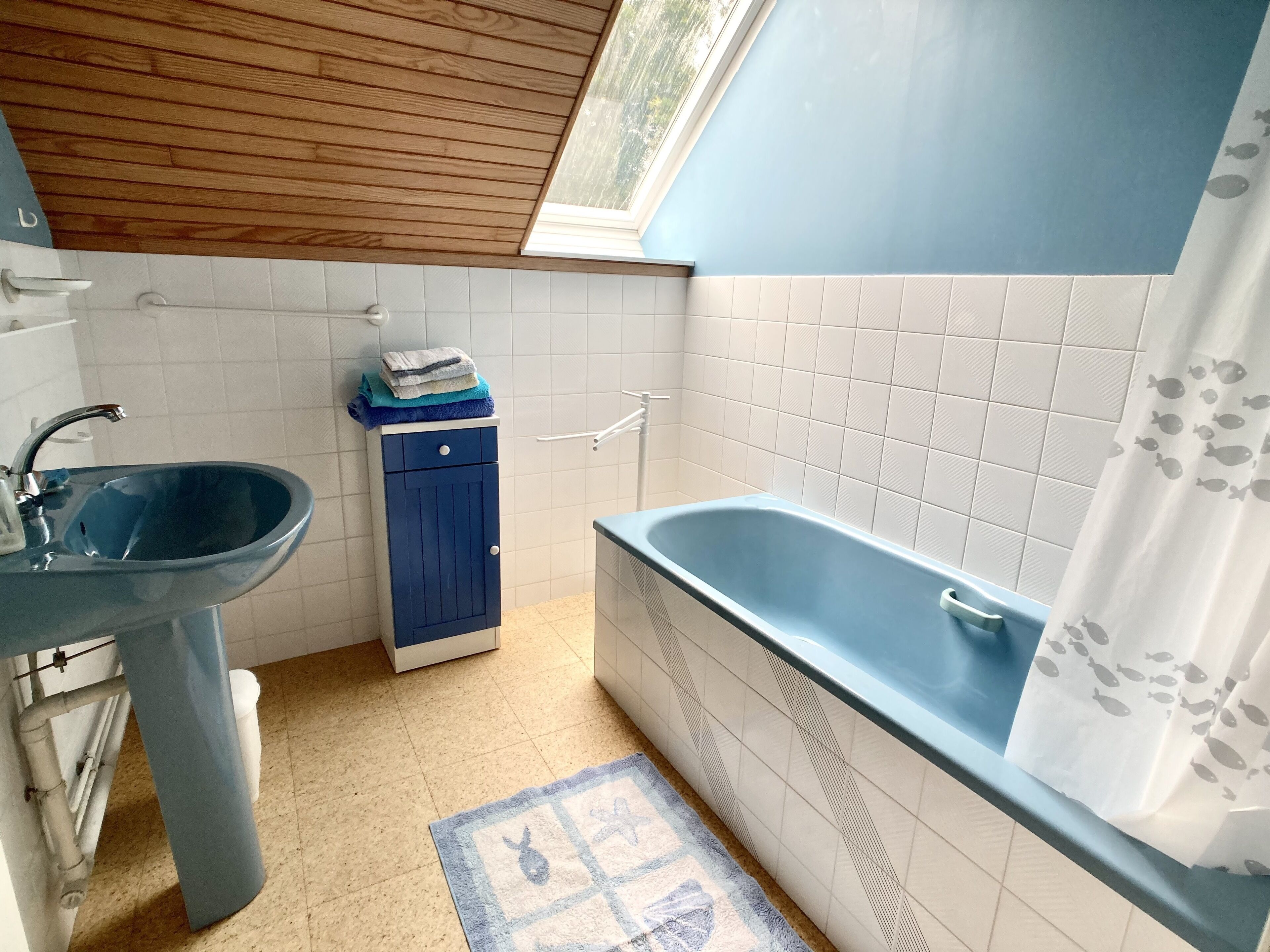 A bathroom with a blue sink, a blue cabinet, a bathtub, and a window above the sink.