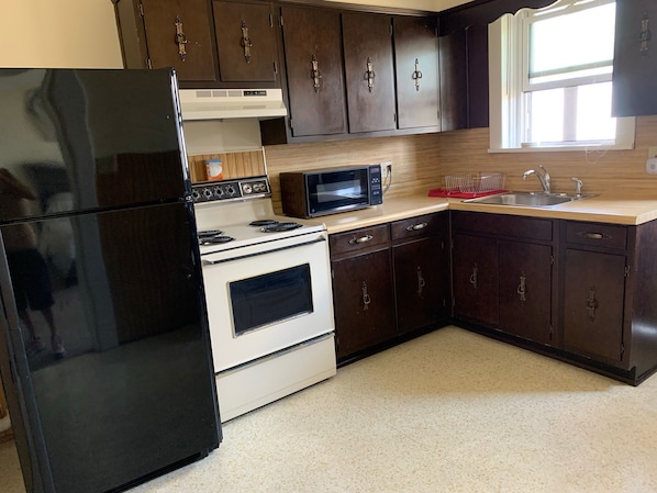 Compact kitchen with a refrigerator, stove, microwave, and sink, complete with dark brown cabinetry and a light-colored countertop.