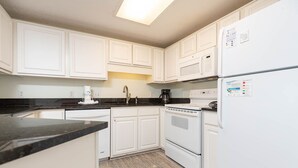 Una cocina con gabinetes blancos, una encimera negra, una estufa y un refrigerador.