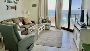 Un salón con sofá, sillón, mesa de centro y vista al océano desde un balcón.