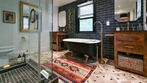A modern bathroom with a black tiled wall, a freestanding bathtub, a wooden vanity, and a patterned rug.