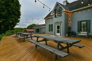 Una terraza de madera con mesas de picnic y luces colgantes.