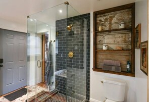 Bathroom features a glass-enclosed shower and a wooden shelf with toiletries.
