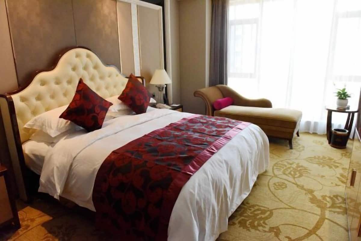 A hotel room with a large bed, a chair, a small table, and a potted plant.