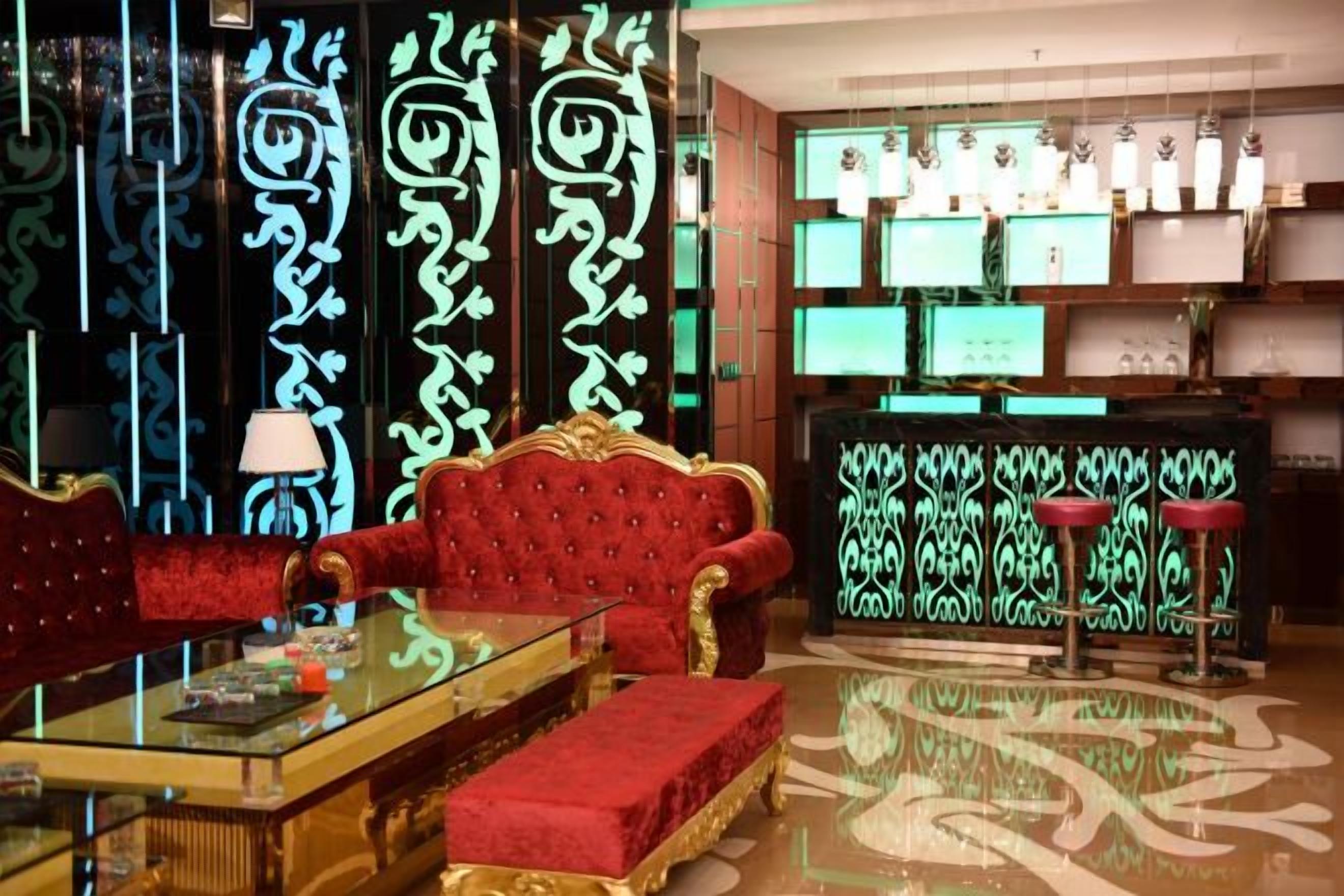 A room with a red upholstered sofa, a glass coffee table, and a patterned floor. There are shelves with decorative items and a bar area with stools.
