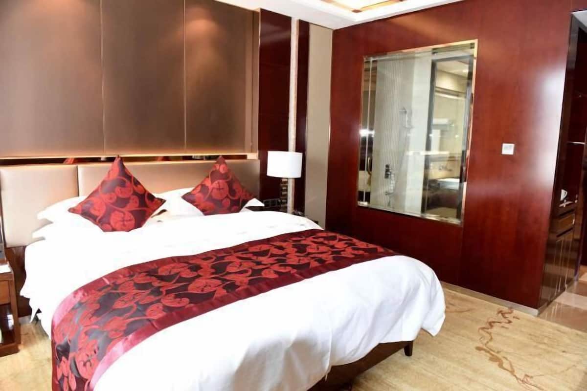 A hotel room with a large bed, a wooden headboard, a mirror, and a nightstand with a lamp.