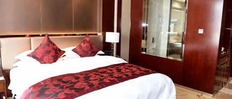 Una habitación de hotel con una cama grande, cabecera de madera, un espejo y una mesita de noche con lámpara.