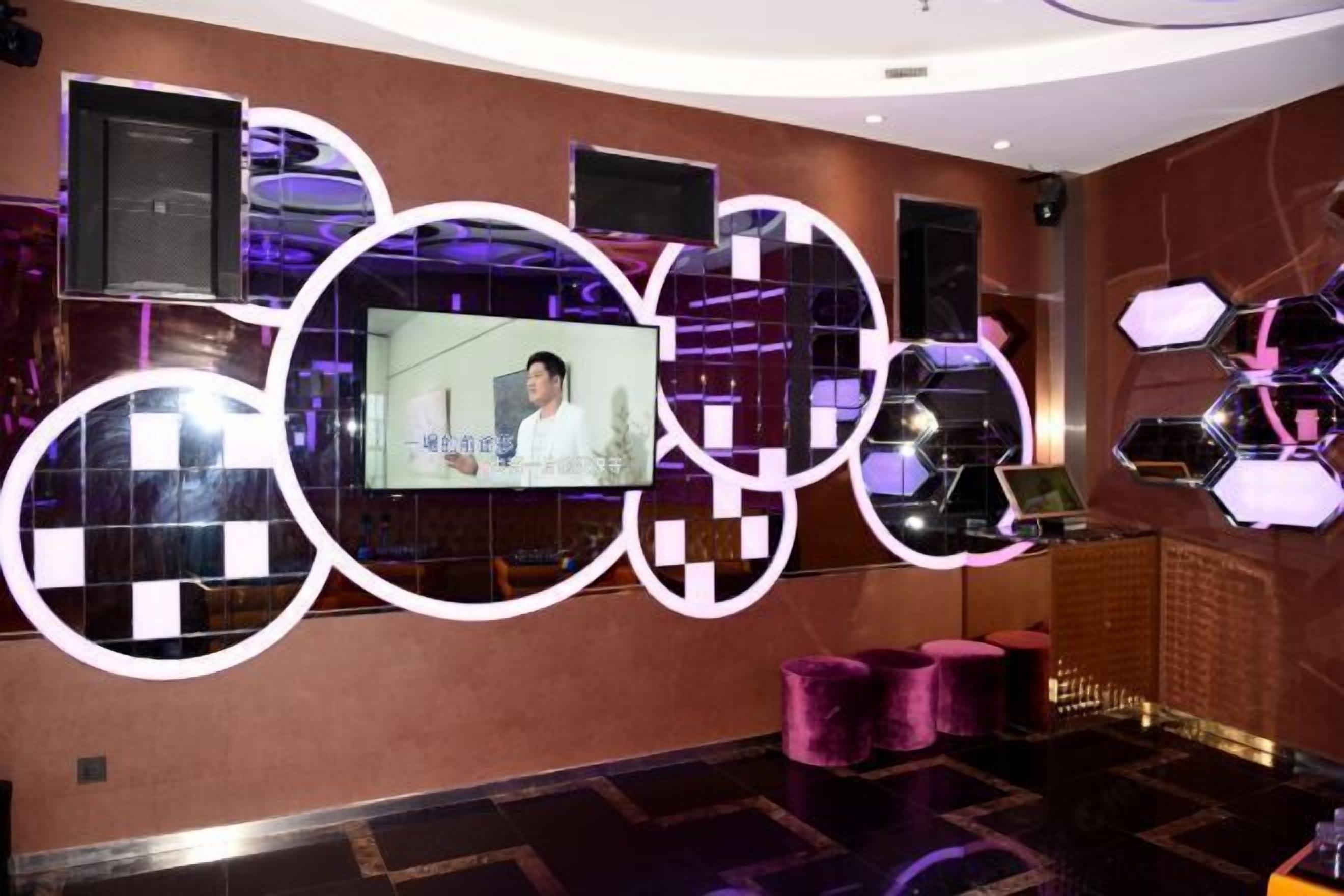 A modern lobby with a large screen displaying a person, circular wall decorations, and a seating area with cushioned stools.