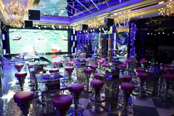 A bar area with multiple high stools and a large screen displaying a sports game.