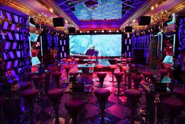 A bar area with multiple stools, a large screen, and decorative lighting.