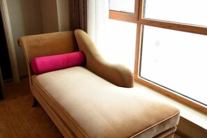 Una cama individual con cabecera, una ventana con marcos de madera y suelo cubierto de alfombra.