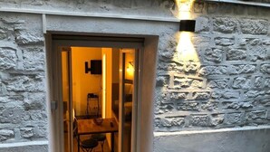 A doorway leading to a room with a table and chairs, a wall-mounted light fixture, and a stone wall. - Apartment 19 rue Gutenberg (Paris)