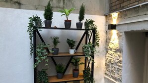 A black metal shelving unit with potted plants, a white mug, and a brick wall in the background. - Apartment 19 rue Gutenberg (Paris)
