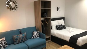 A room with a blue sofa, a wooden table, a bed with white bedding, and a wardrobe. - Apartment 19 rue Gutenberg (Paris)