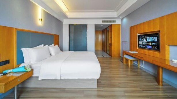 A modern hotel room with a large bed, a wooden headboard, a flat-screen TV, a wooden bench, and a desk with a lamp. - Dongting Hotel (Nan County)