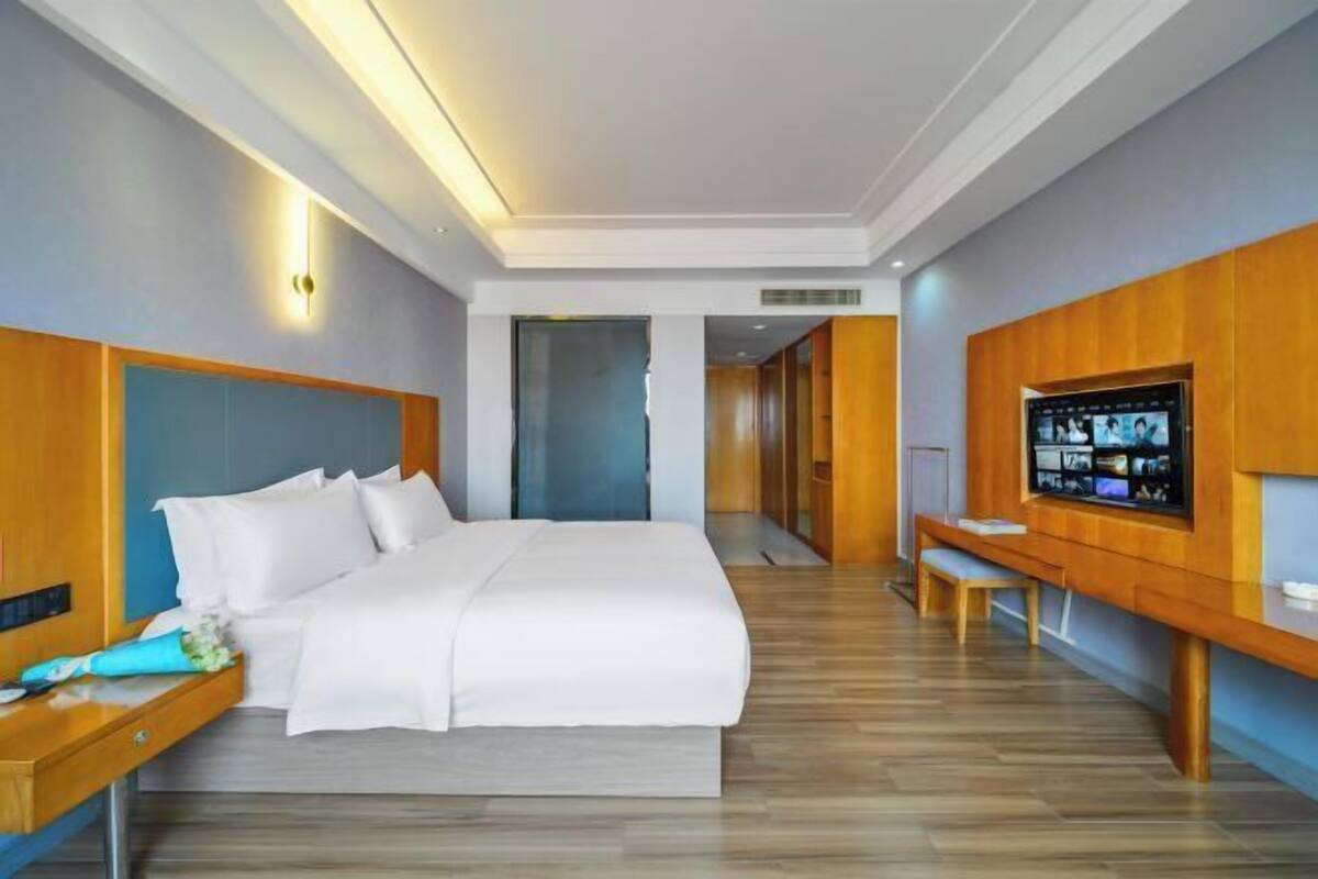 Een moderne hotelkamer met een groot bed, een houten hoofdeinde, een flatscreen televisie, een houten bankje en een bureau met een lamp.