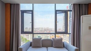 A room with a sofa, a window with curtains, and a view of a cityscape. - Dongting Hotel (Nan County)