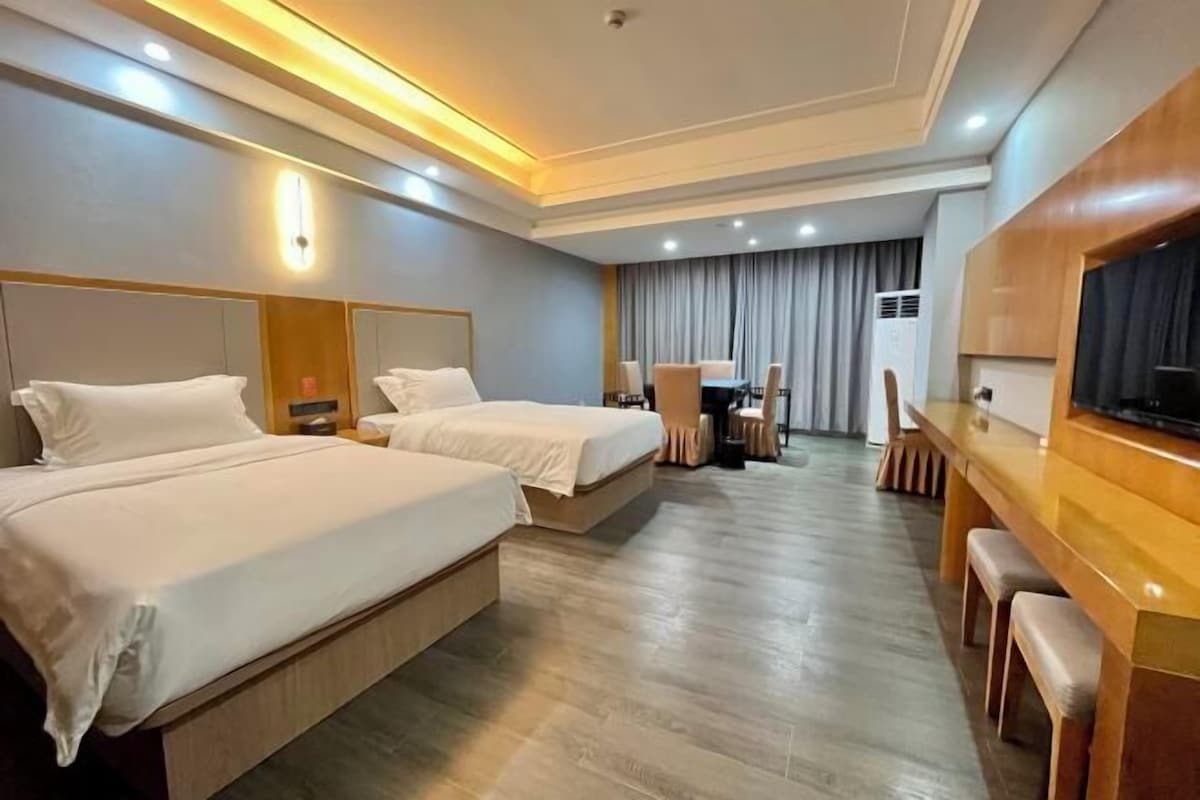A hotel room with two beds, a desk, a TV, and a dining area.