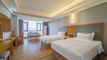 A hotel room with two beds, a desk, a chair, and a view of the city.