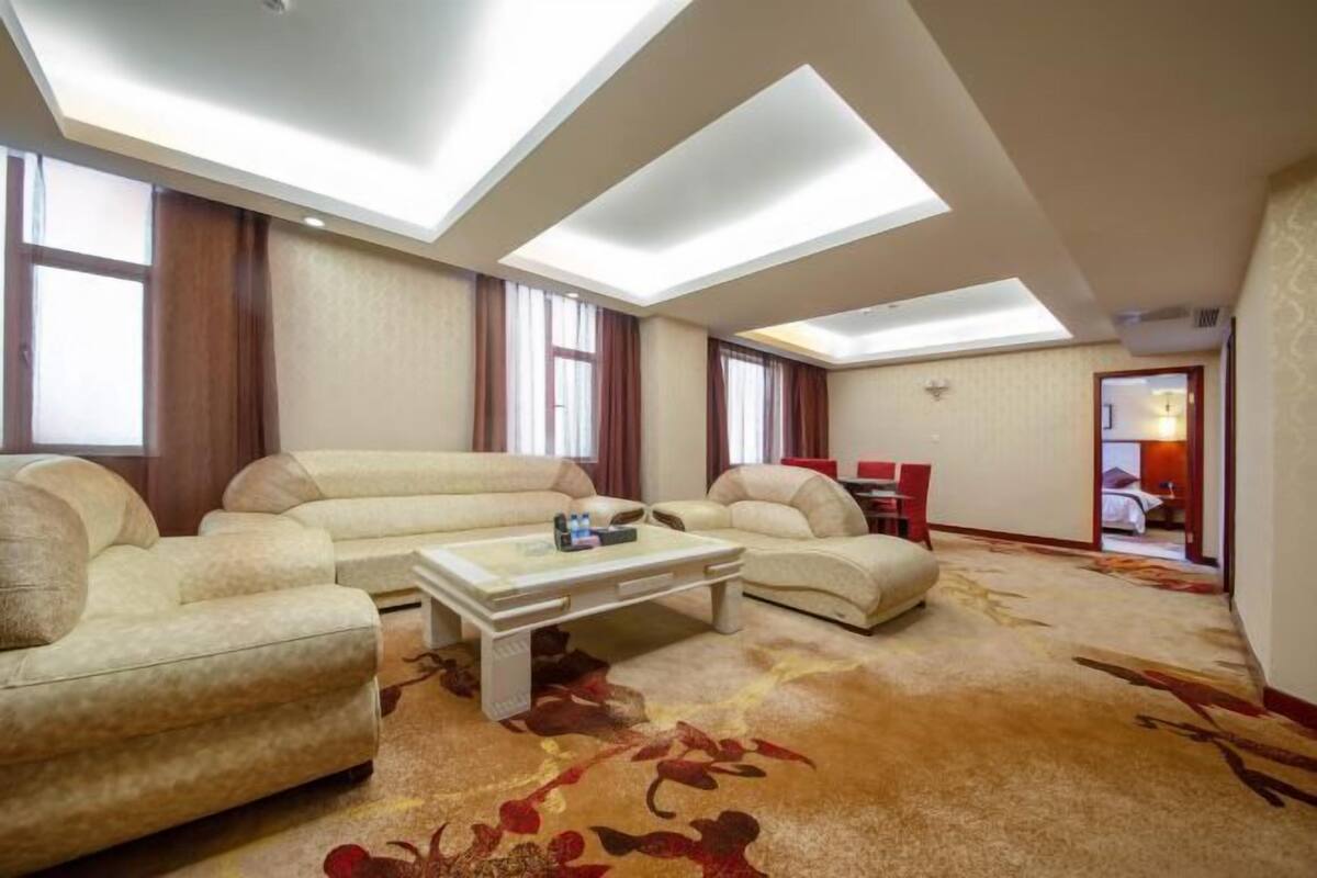Een ruime woonkamer met een hoge plafond, grote ramen en een centrale salontafel.