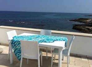 Relax in this serene outdoor seating area overlooking the water, featuring a table and comfortable wicker chairs.