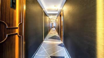 A hotel corridor with a geometric patterned floor, wooden doors, and a modern ceiling design.