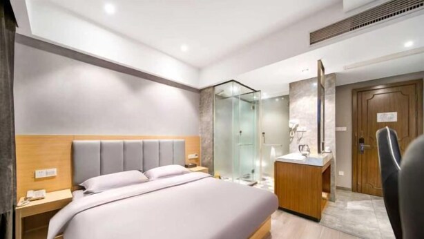 Una habitación de hotel moderna con una cama grande, cabecera de madera, box de ducha de vidrio, tocador de madera y un espejo.