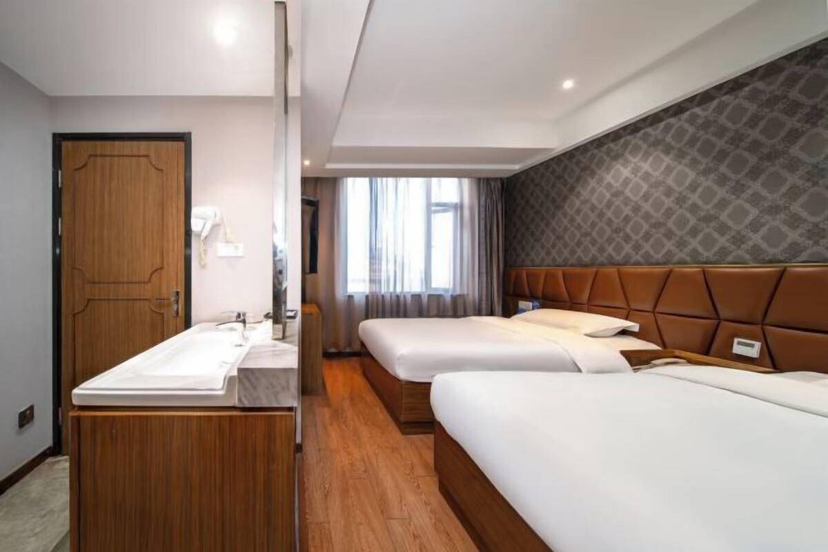 Ein Hotelzimmer mit zwei Betten, einem Holzkleiderschrank, einem Badezimmer mit Waschbecken und einem Fenster mit Vorhängen.